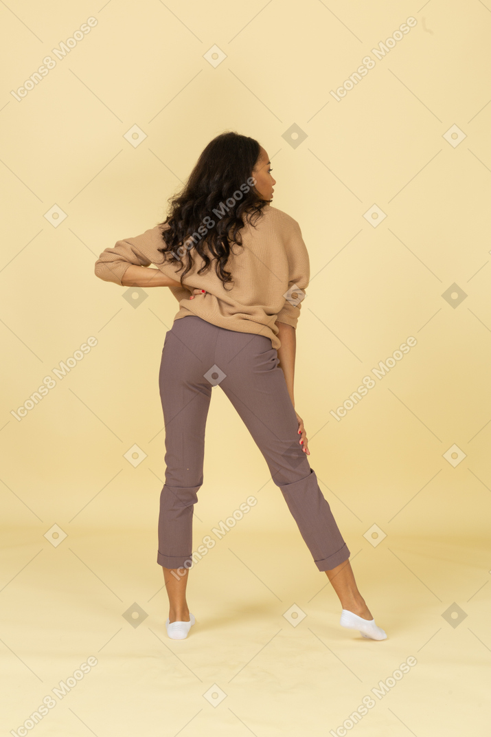 Back view of a dark-skinned young female putting hand on hip while looking aside