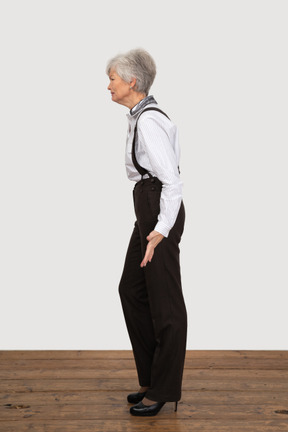 Side view of a grimacing old lady in office clothing outspreading her hands