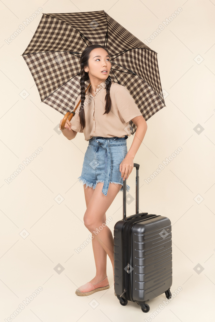 Young woman with umbrella and suitcase looking at the sky