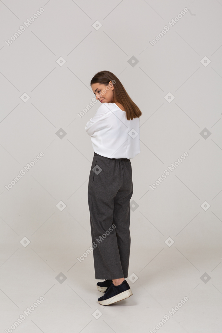 Vista posteriore di tre quarti di una giovane donna sorridente in abiti da ufficio che inclina la testa
