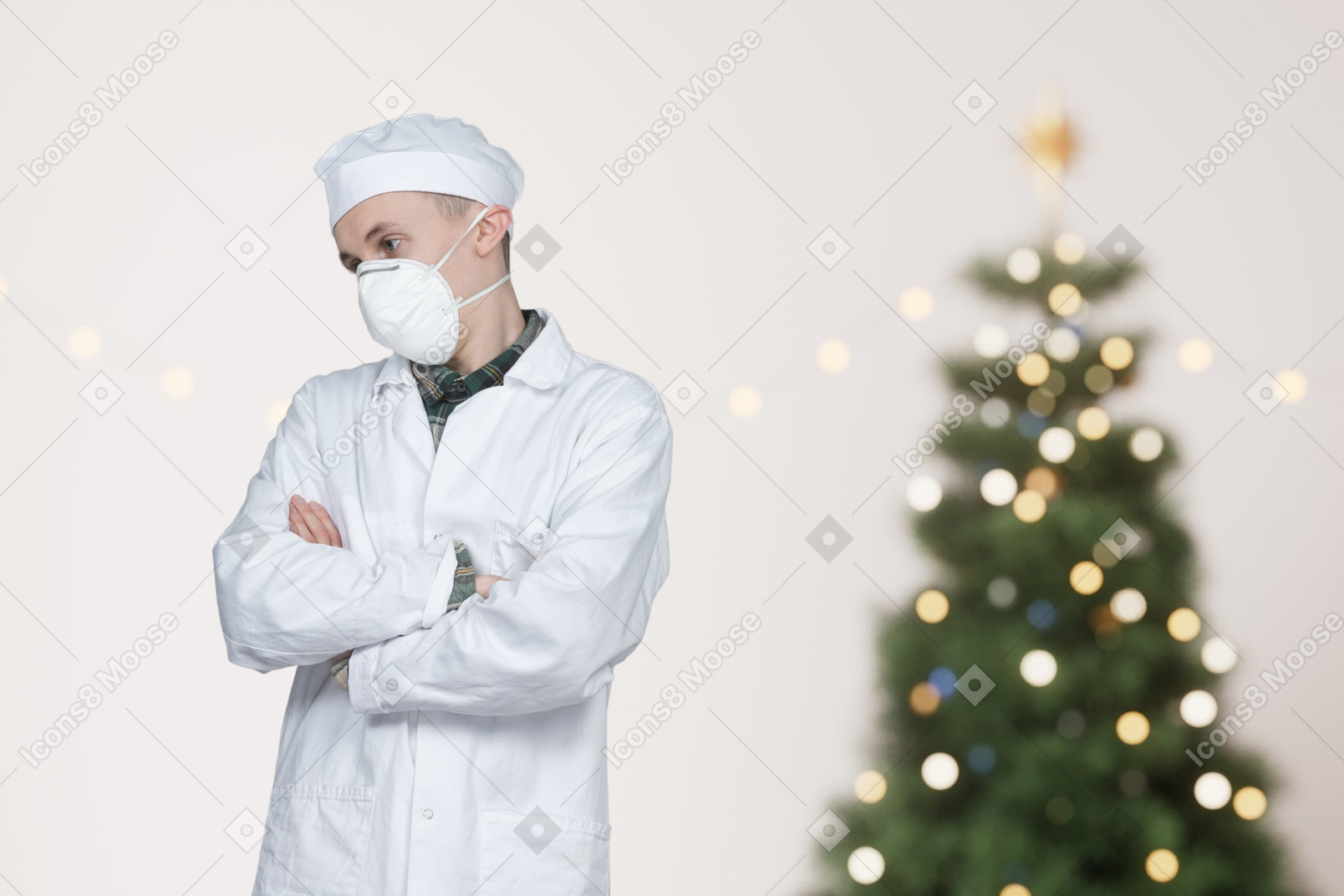 A man wearing a surgical mask standing in front of a christmas tree