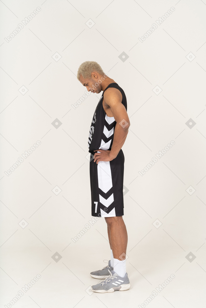 Вид сбоку тренирующегося молодого баскетболиста мужского пола, положившего руки на бедра