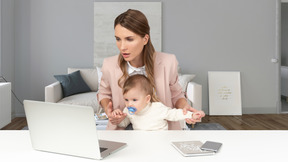 A woman holding a baby in front of a laptop