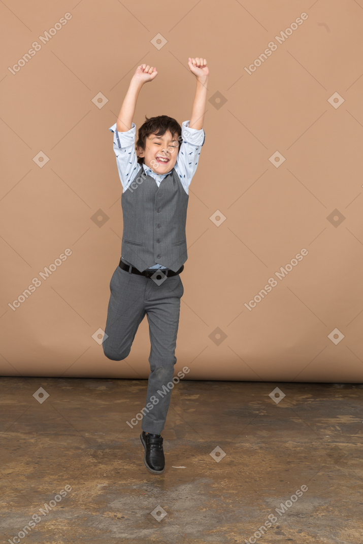 Вид спереди на симпатичного мальчика в костюме, прыгающего с вытянутыми руками