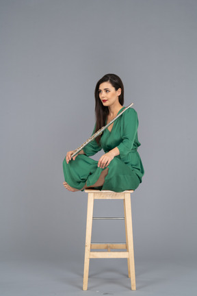 Full-length of a young lady holding the clarinet sitting with her legs crossed on a wooden chair