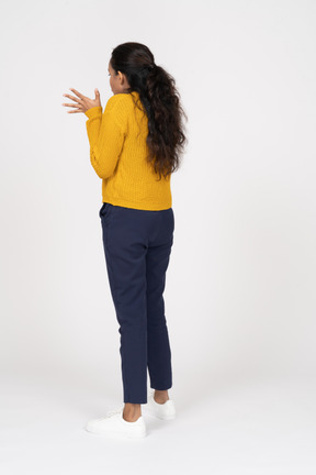 Вид сзади эмоциональной девушки в повседневной одежде, стоящей с поднятыми руками