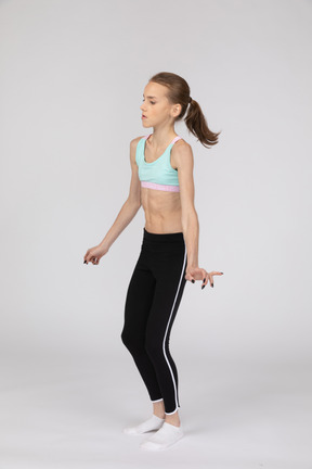 Three-quarter view of a teen girl in sportswear outspreading hands and bending knees