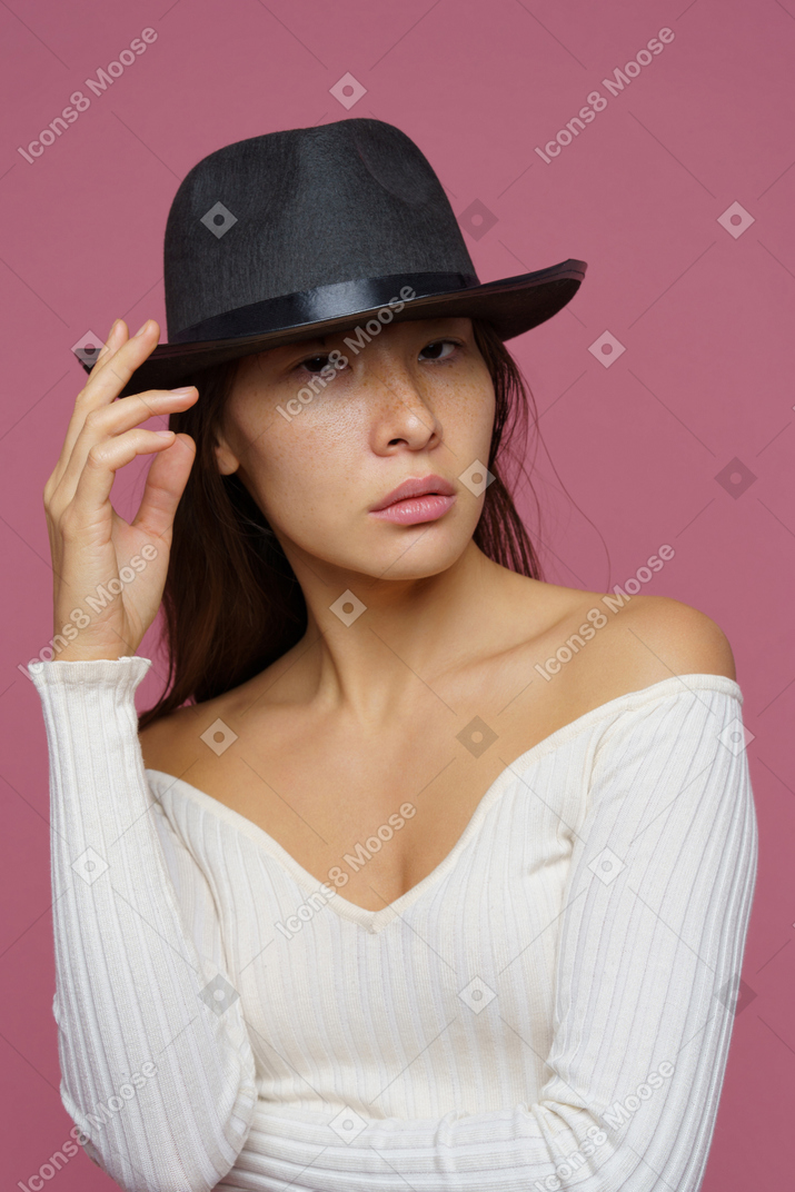 Vue de face d'une jeune femme autoritaire touchant élégamment son chapeau noir
