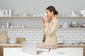 A woman sitting on a kitchen counter drinking from a mug
