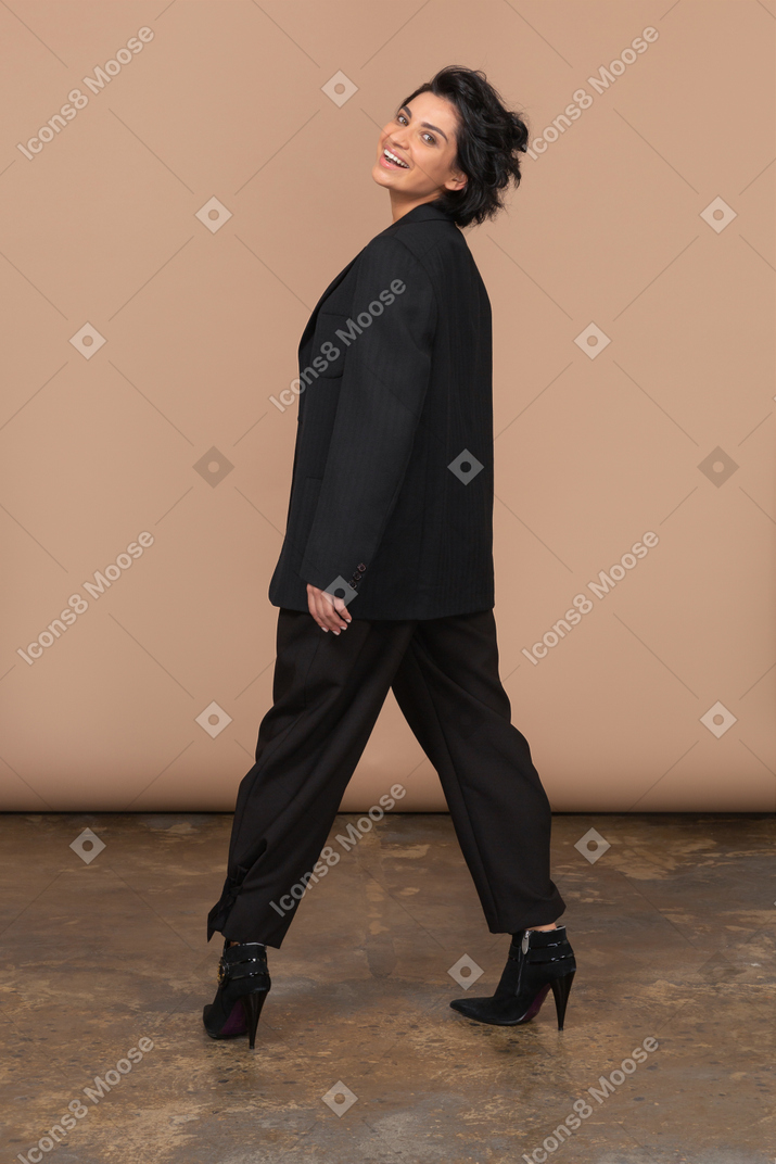 Vista traseira de uma mulher de negócios feliz vestindo um terno preto, olhando para a câmera e sorrindo