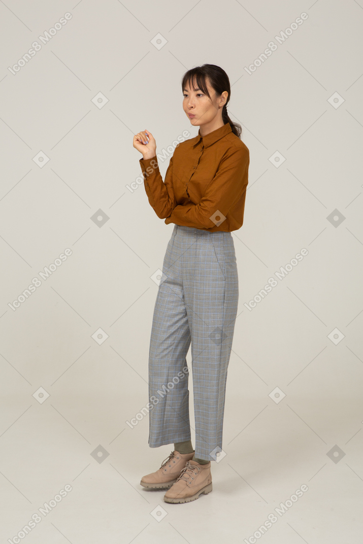 Vista di tre quarti di una giovane donna asiatica in calzoni e camicetta che alza la mano
