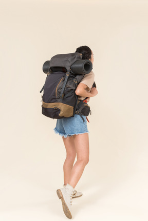 Young female hiker carrying heavy backpack and standing back to camera