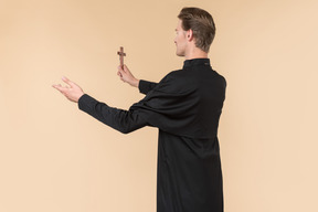 Catholic priest standing half sideways back to camera and holding cross