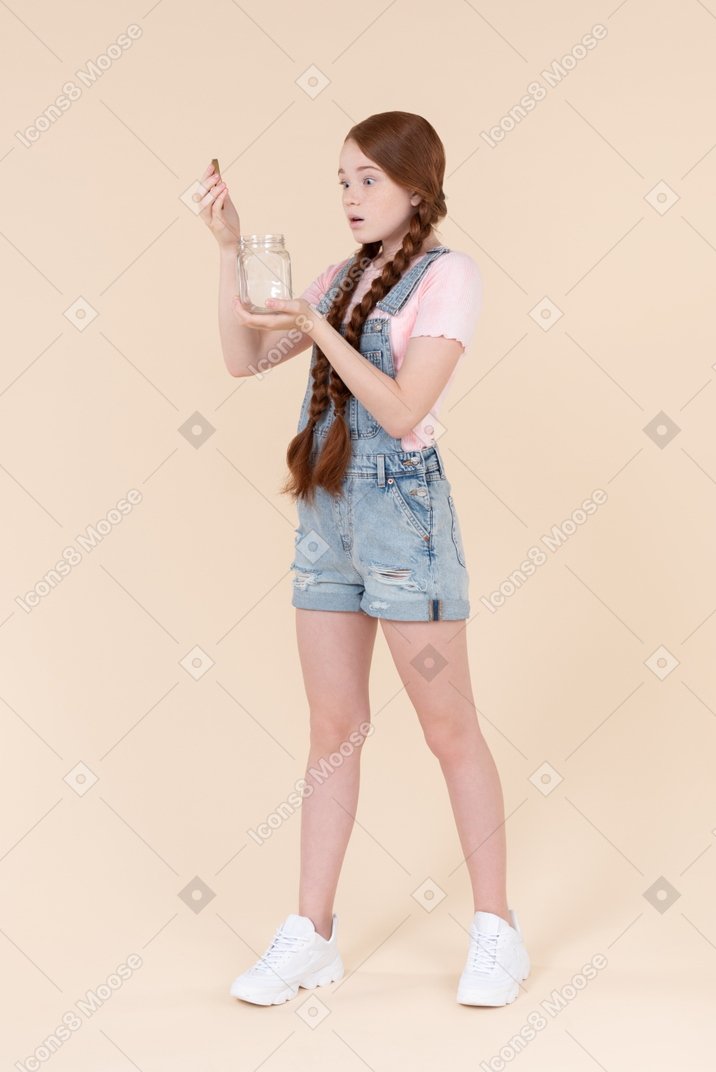 Teenage girl looking closely into the jar she's holding