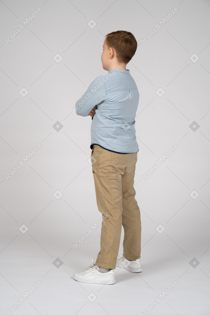 Vista lateral de um menino fofo em pé com os braços cruzados