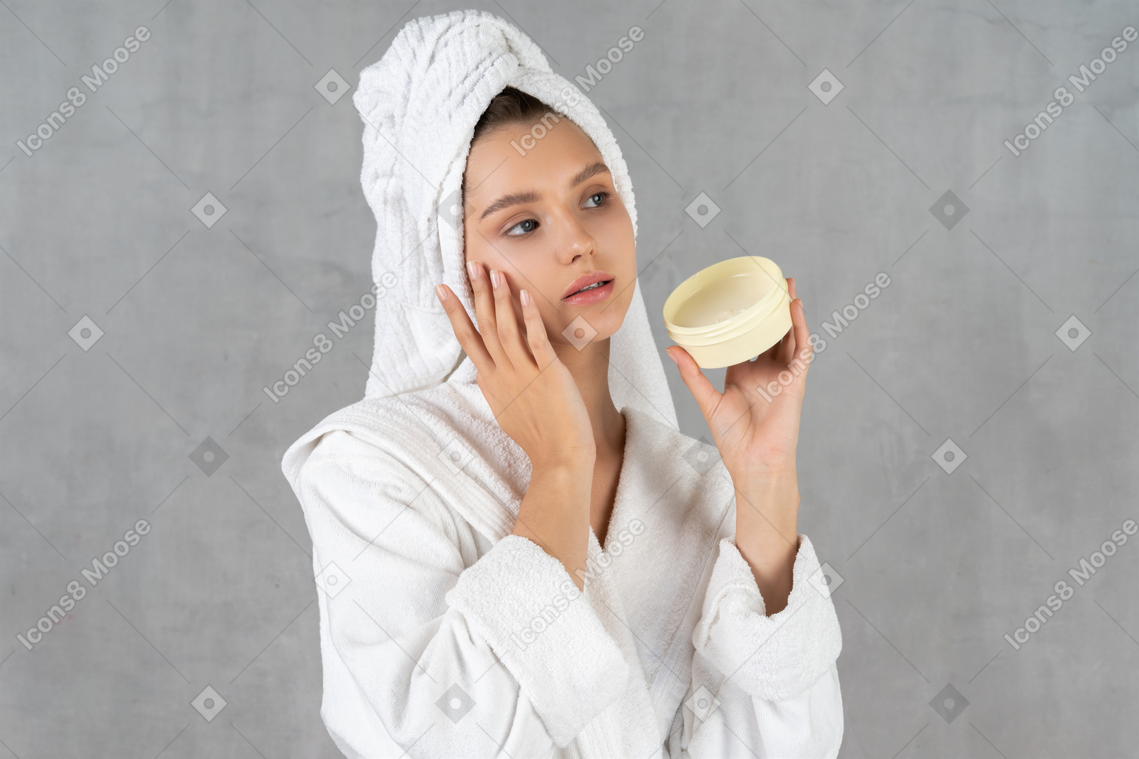 Woman in bathrobe touching cheek and holding a tub of cream