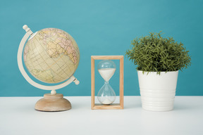 Globe, hourglass and house plant on a blue background