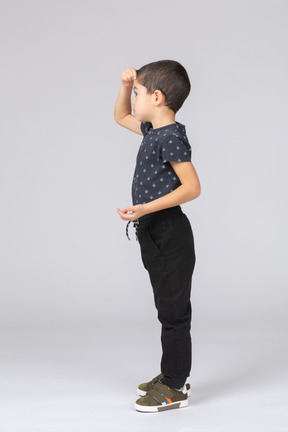 Vista lateral de un niño en ropa casual posando con las manos en la cabeza.