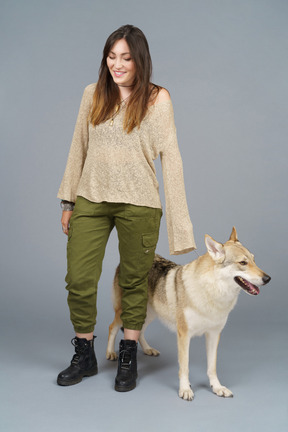 Pleine longueur d'un maître féminin souriant regardant vers le bas et debout près de son chien