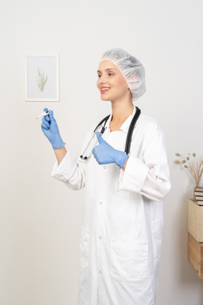 Three-quarter view of a smiling young female doctor with stethoscope holding thermometer and showing thumb up