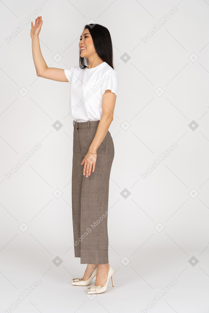 Three-quarter view of a greeting young woman in breeches raising her hand
