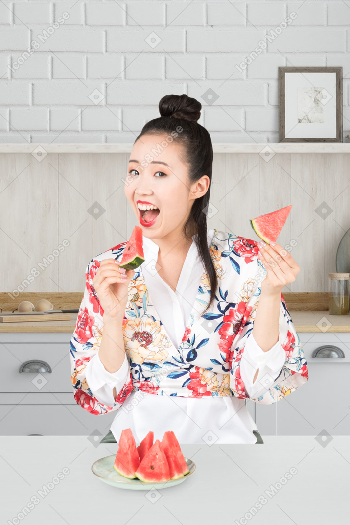 Mulher asiática comendo melancia na cozinha