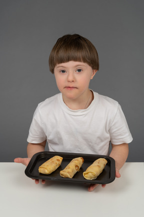 Portrait of a little boy holding spring rolls on a tray