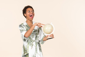 Black short-haired woman in a white and green dress, standing with a globe in her hand