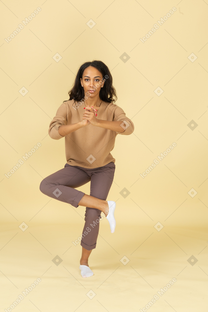 Vista frontal de una mujer joven de piel oscura en cuclillas de pie sobre una pierna
