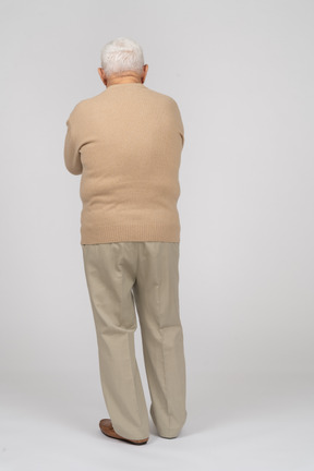 Rear view of an old man in casual clothes standing with crossed arms