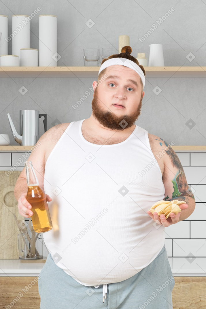 A man in sportswear holding a bottle of beer and chips in his hand