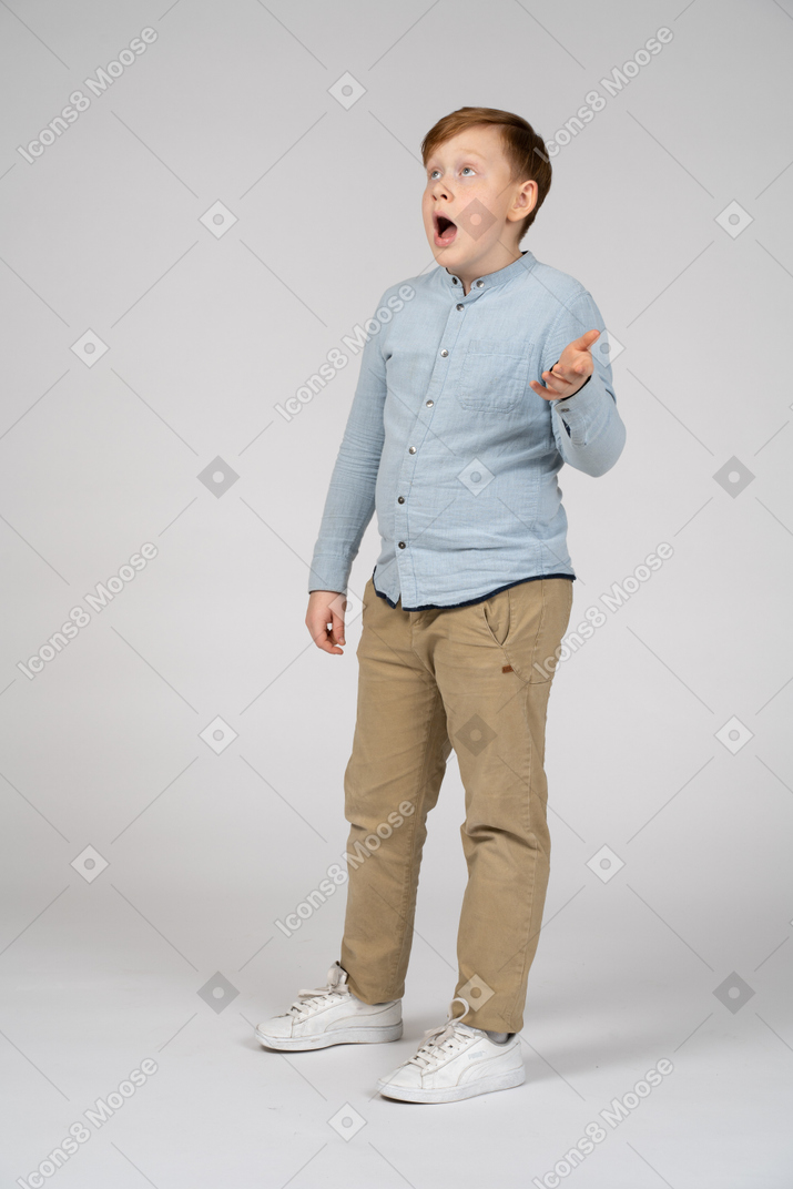 Surprised boy in blue shirt and khaki pants looking up