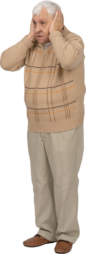Vista frontal de un anciano con ropa informal que cubre las orejas con las manos