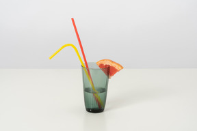 A glass of cold water with a slice of grapefruit on it, with two colorful plastic straws