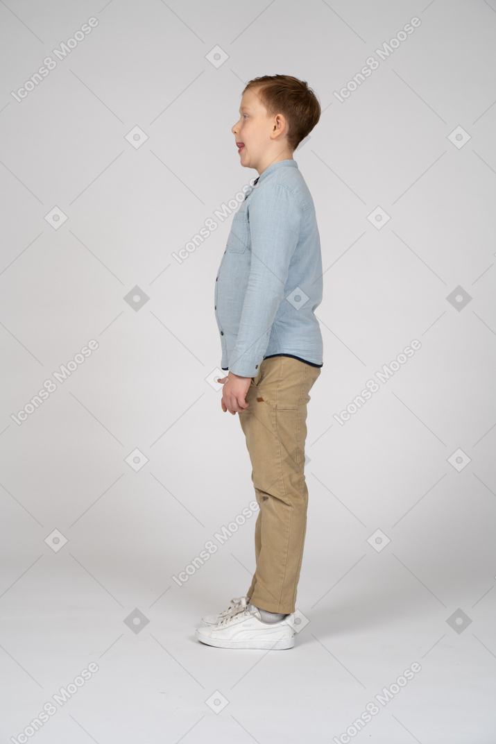 Side view of a cute boy in casual clothes making faces