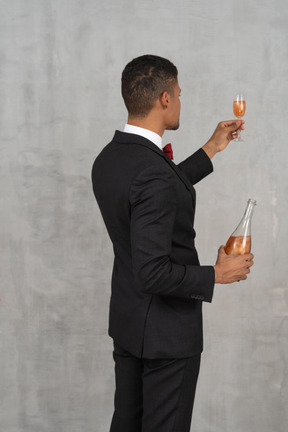 Vue arrière du jeune homme tenant une bouteille d'alcool et un verre de flûte