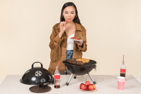 Young asian woman standing near grill and throwing a fruit