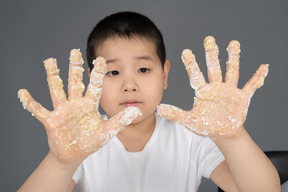 Um menino surpreso, olhando para as mãos farinhas