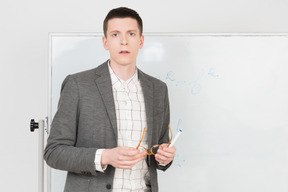 Young attractive teacher holding his eyeglasses and looking right in the camera