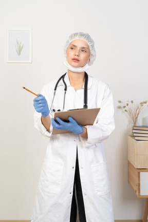 Front view of a puzzled young female doctor making notes on her tablet