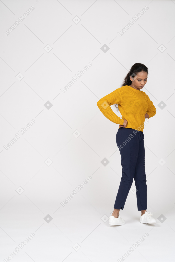 Vista lateral de una chica en ropa casual posando con las manos en las caderas y mirando hacia abajo