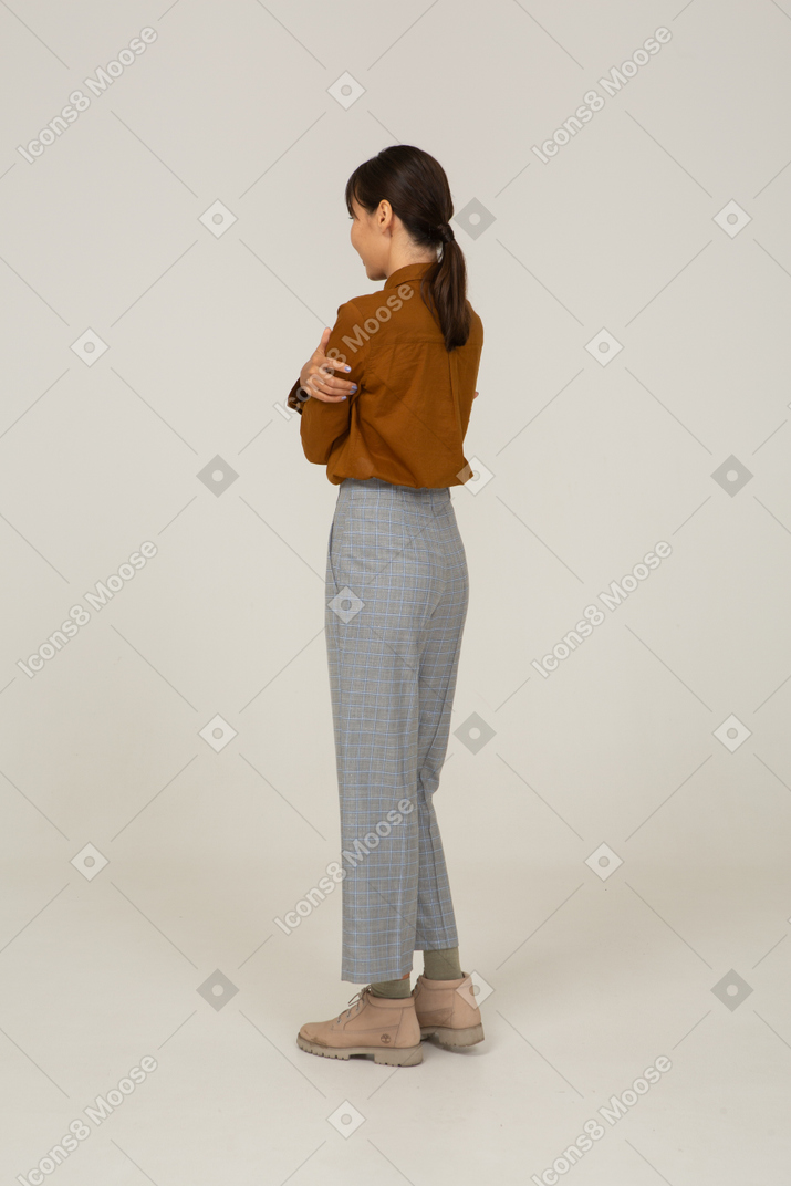 Three-quarter back view of an offended young asian female in breeches and blouse crossing arms