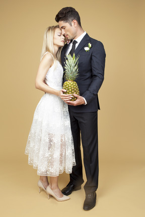 Bride and groom standing shoulder to shoulder and holding a pineapple