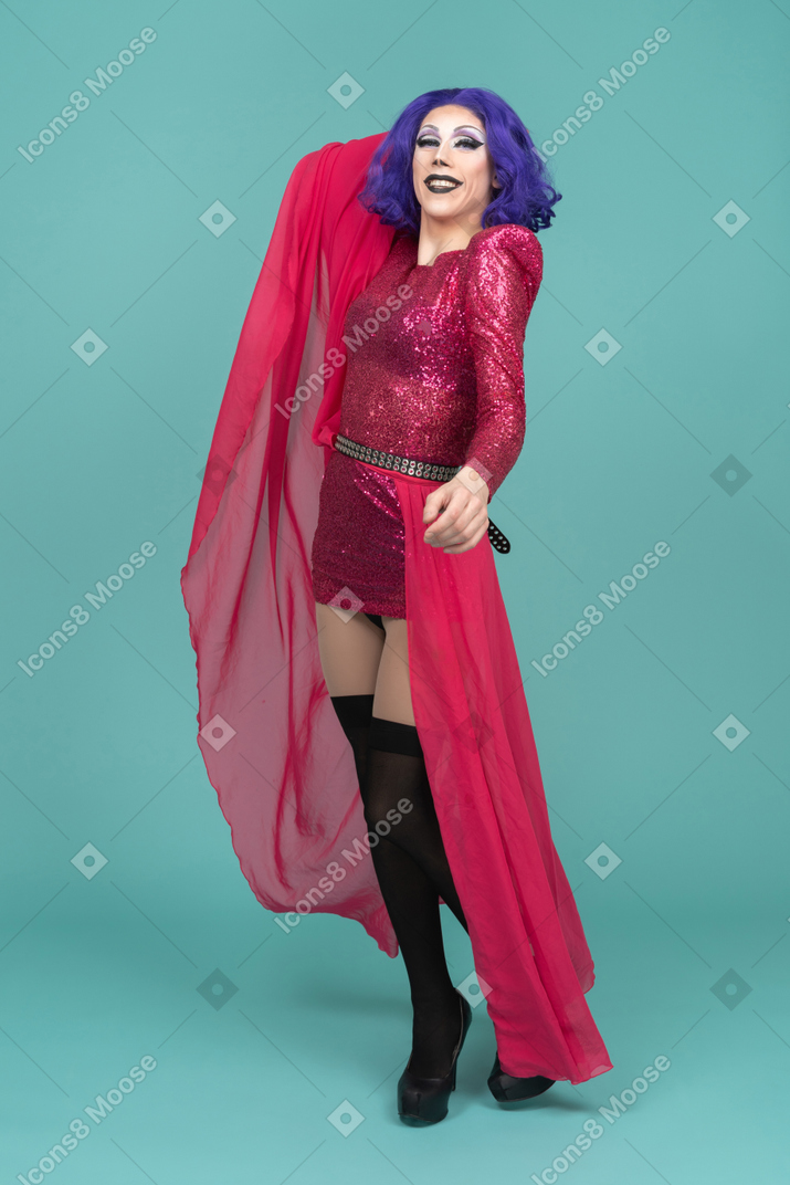 Drag queen de vestido rosa sorrindo e levantando a saia até a cabeça