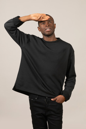 Front view of a young man standing with hand on forehead and looking up