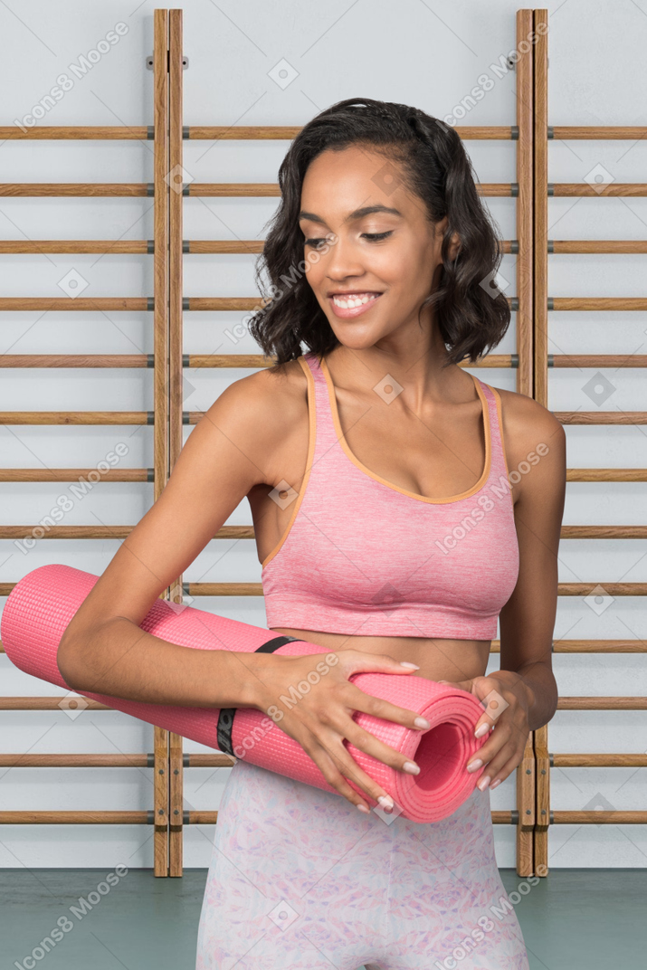 A woman holding a pink yoga mat in a gym