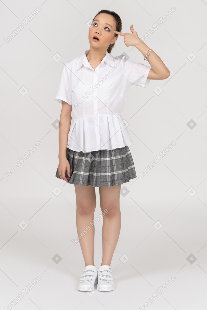 Engraçada menina asiática segurando uma arma de dedo ao lado de sua cabeça