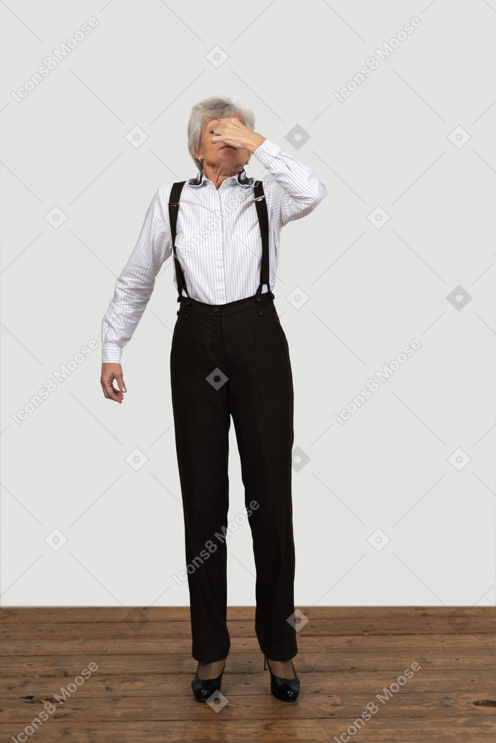 Front view of an old female in office clothes sneezing indoors