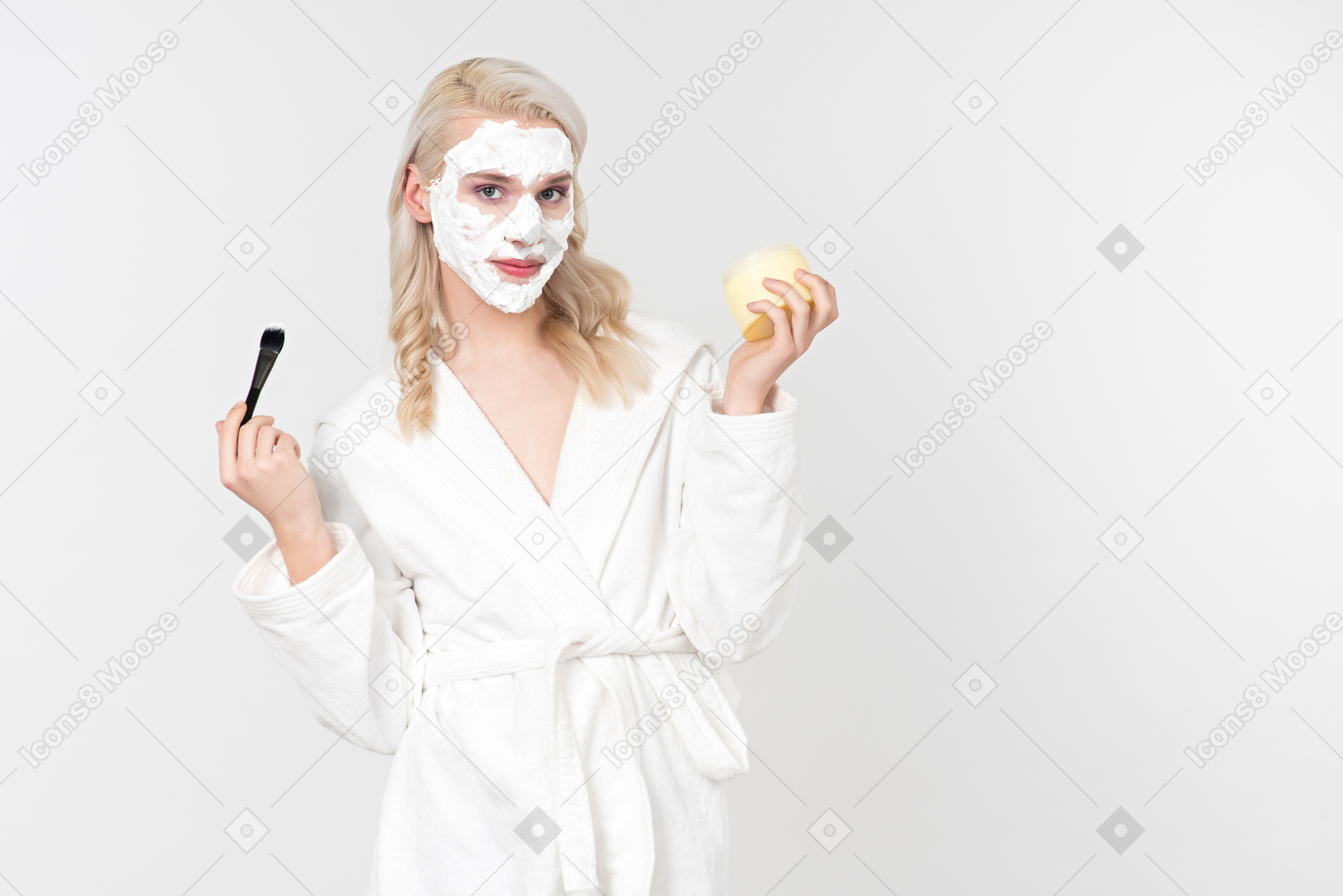 A good looking blond-haired young man in a white bathrobe, being in the process of his beauty care routine