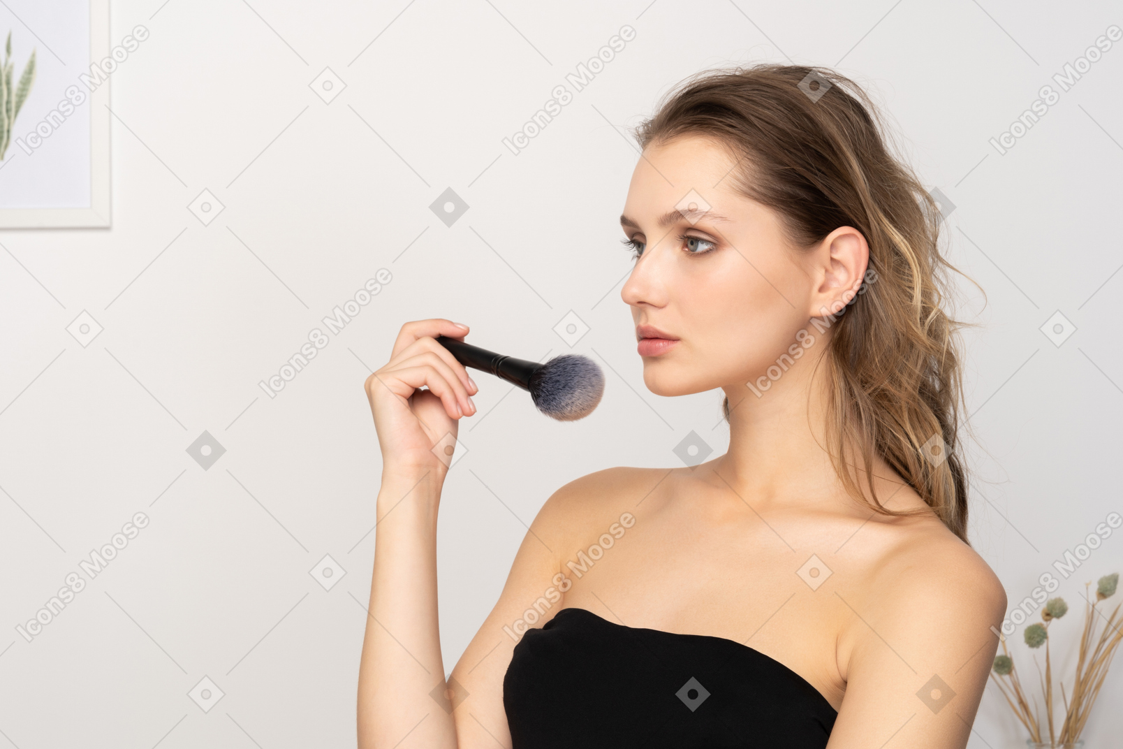 Vista de tres cuartos de una mujer joven sensual sosteniendo un pincel de maquillaje